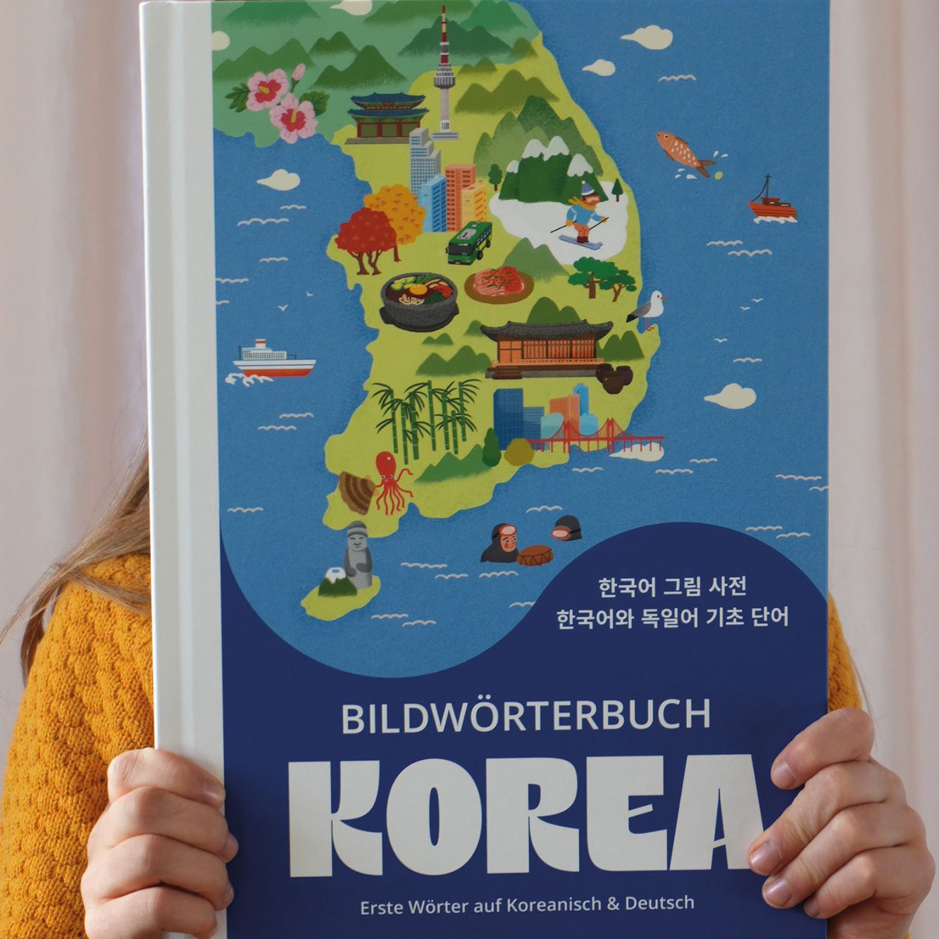 Ein Bild von einem Kind, dass das Cover vom Bildwörterbuch Korea in die Höhe hält.
